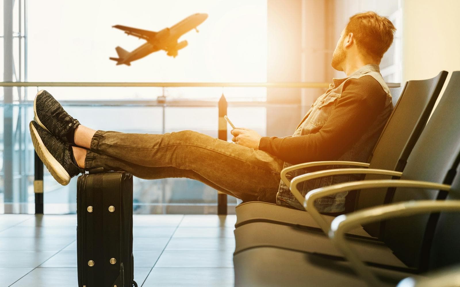A passenger waits at the gate with his feet up on his suitcase