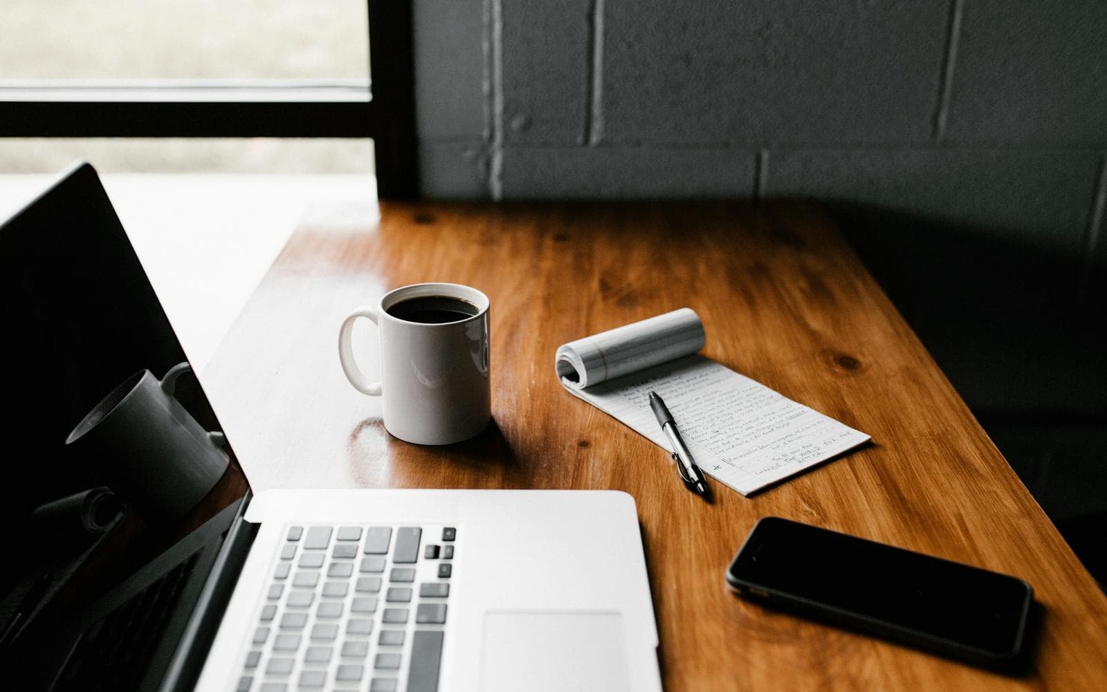 A laptop, a coffee and a notepad on a desk