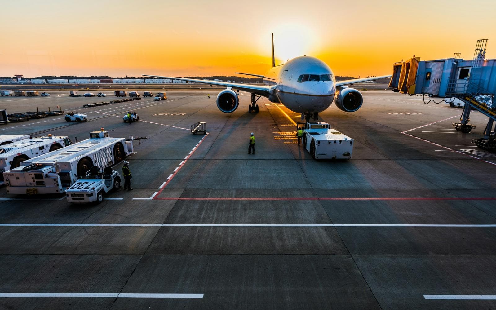 A plane parked at the gate at sunrise, with ground crew around it